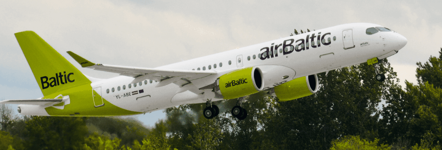 An airBaltic aircraft with green and white livery takes off, ascending into the sky with trees in the background